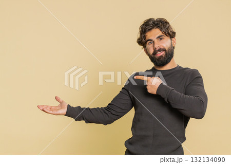 Lebanese young man showing thumbs up and pointing at empty blank place against beige background 132134090