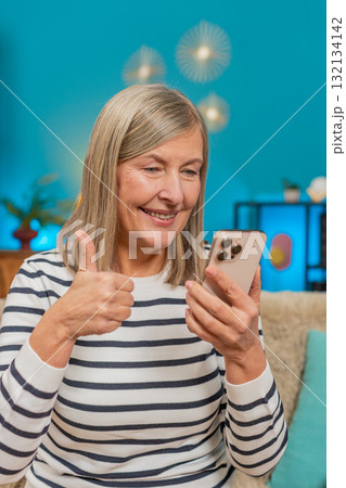 Mature woman celebrating online lottery win victory on smartphone, happily viewing good news at home 132134142