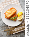 Saganaki is a Greek appetizer consisting of pan-fried cheese served with a lemon wedge, close-up on a plate. Vertical top view 132134970