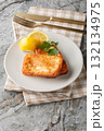 Light Greek appetizer Saganaki of fried cheese served with a lemon wedge close-up in a plate. Vertical 132134975