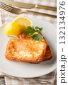 Saganaki is a Greek appetizer consisting of pan-fried cheese served with a lemon wedge, close-up on a plate. Vertical 132134976