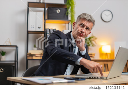 Young businessman using laptop while thinking about important creative project decision at desk Young businessman using laptop while thinking about important creative project decision at desk 132135141