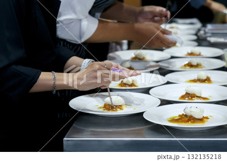 chefs in a professional kitchen garnishing dessert plates with precision. restaurant chef team showcasing fine dining presentation, culinary creativity, and teamwork in food preparation. 132135218