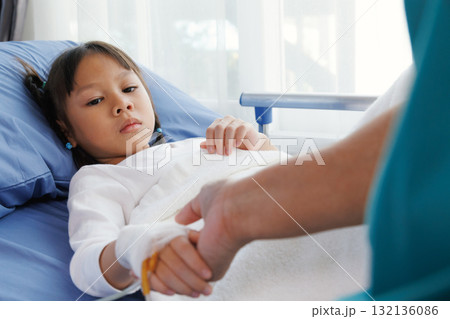 asian girl patient lying in hospital bed with bandaged hand and IV line, holding hands with nurse, doctor, medical professional or father. healthcare with compassion, trust and emotional support. 132136086