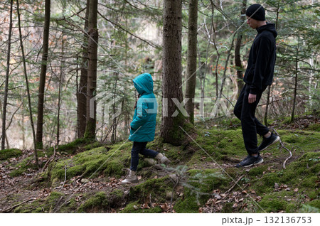 Exploring a tranquil forest trail with a child during autumn, surrounded by lush greenery and fallen leaves under a soft natural light Exploring a tranquil forest trail with a child during autumn, surrounded by lush greenery and fallen leaves under a soft natural light 132136753