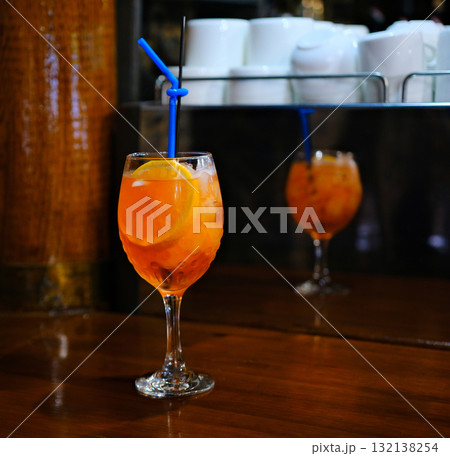 Aperol alcoholic drink wine glass with slices of orange and ice cubes inside. On a terrace of a city cafe, Minsk, Belarus. Greenery in the background, 132138254