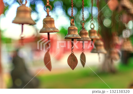Antique bronze bells hang from chains against a backdrop of greenery and soft bokeh. 132138320