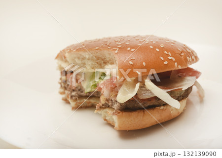 A nibbled hamburger with meat and vegetables. Fast food. Hamburger on a plate. Fast food scraps. A nibbled hamburger with meat and vegetables. Fast food. Hamburger on a plate. Fast food scraps. 132139090