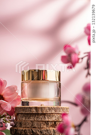 Glass cosmetic cream jar with gold lid and pink flowers on wood 132139679