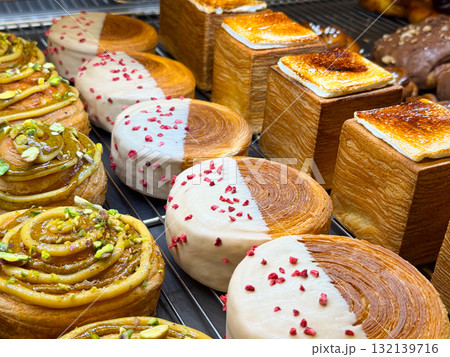 Pistachio rolls, round buns with icing, and caramelized cubes arranged on bakery rack. Dessert composition representing creativity, craft, and culinary art. Pistachio rolls, round buns with icing, and caramelized cubes arranged on bakery rack. Dessert composition representing creativity, craft, and culinary art. 132139716