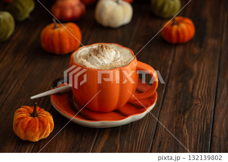 Cozy pumpkin latte in a pumpkin-shaped mug with whipped cream and spices, surrounded by autumn decor. Cozy pumpkin latte in a pumpkin-shaped mug with whipped cream and spices, surrounded by autumn decor. 132139802