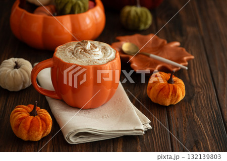 Cozy pumpkin latte in a pumpkin-shaped mug with whipped cream and spices, surrounded by autumn decor. 132139803