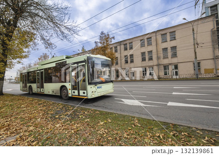 Green electric bus driving down the street on a cloudy autumn day near an old building Green electric bus driving down the street on a cloudy autumn day near an old building 132139861