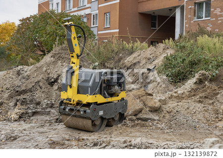 Construction site with a small vibrating roller compacting dirt near residential buildings in autumn 132139872