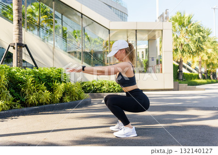 Fit woman performs challenging sport exercise workout outdoor, doing squats for strength training amidst modern city environment, fit individual embracing active healthy lifestyle for people. 132140127