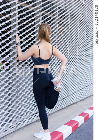 Fit woman, sport exercise workout for people, stretching outdoor, showing dedication to healthy active lifestyle, maintaining fit body against contemporary geometric wall. 132140129