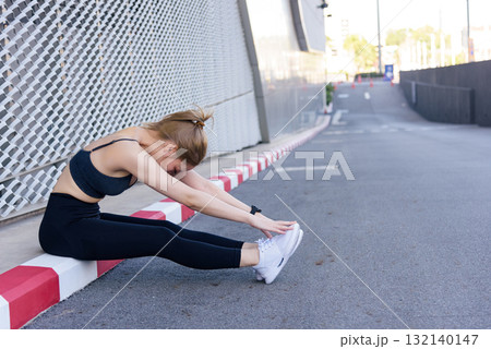 Workout woman performs outdoor sport exercise, stretching fit body for flexibility, enjoying active workout on urban street curb beside modern building for healthy lifestyle. Workout woman performs outdoor sport exercise, stretching fit body for flexibility, enjoying active workout on urban street curb beside modern building for healthy lifestyle. 132140147