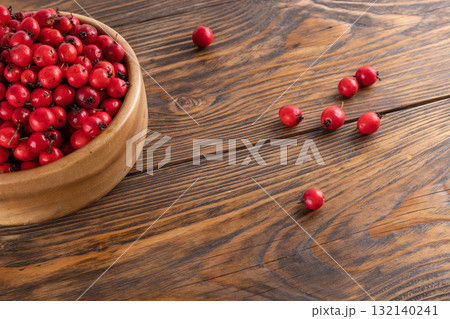 red hawthorn berries in wooden bowl on flat wooden surface 132140241