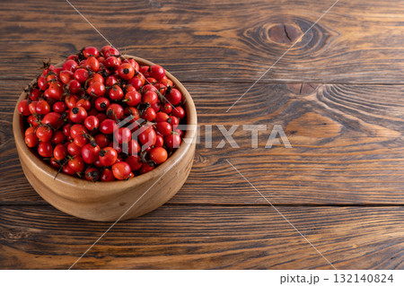 red dog-rose rosehip fruits in a wooden bowl on wooden table 132140824