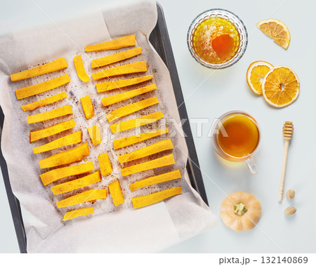 Autumn food. Baked pumpkin slices with cinnamon and honey on a baking sheet with tea and dried fruits on a blue background. Vegan dessert, healthy food. Flat lay Autumn food. Baked pumpkin slices with cinnamon and honey on a baking sheet with tea and dried fruits on a blue background. Vegan dessert, healthy food. Flat lay 132140869