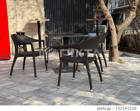 Rattan chairs and small tables arranged on tiled pavement in sunny courtyard. Peaceful scene reflecting urban relaxation and slow rhythm of life. 132141150