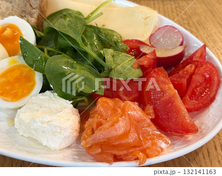Plate with tomatoes, radish, spinach, cheese, and salmon arranged for morning meal. Fresh food composition symbolizing health and culinary balance. 132141163