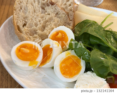 Halved eggs with soft yolk placed beside bread and fresh spinach. Homemade meal expressing comfort, taste, and natural simplicity. 132141164