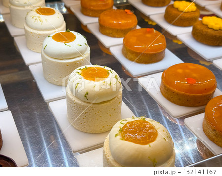 Small mousse cakes with citrus topping placed on white plates. Bakery presentation highlighting detail, structure, and refined pastry craft. 132141167