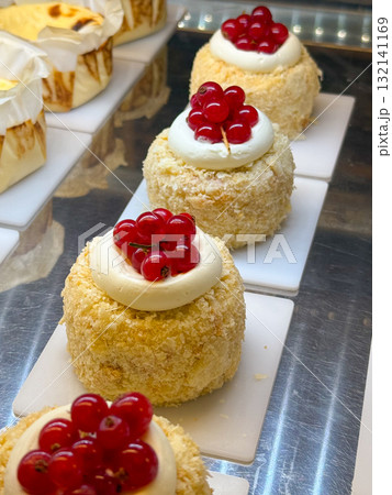 Round pastries with white meringue topping and cakes decorated with red berries arranged on white plates. Bakery display combining cream, color and craft. 132141169