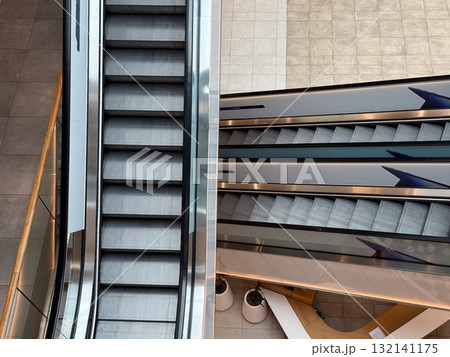 Escalators inside a contemporary shopping center viewed from above. Movement, symmetry, and urban architecture symbolizing daily routine and structure. 132141175