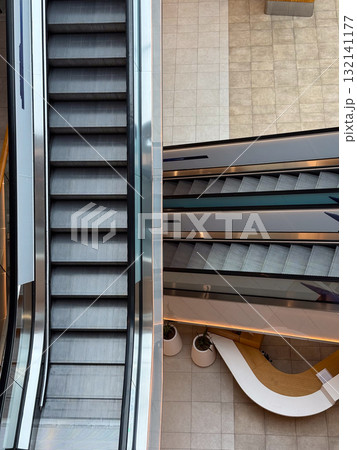 Escalators inside a contemporary shopping center viewed from above. Movement, symmetry, and urban architecture symbolizing daily routine and structure. Escalators inside a contemporary shopping center viewed from above. Movement, symmetry, and urban architecture symbolizing daily routine and structure. 132141177