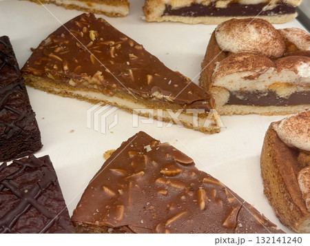Chocolate layered cake slice with almond topping in bakery display. Concept of indulgence, craftsmanship, and sweet temptation through texture and refined dessert presentation. 132141240