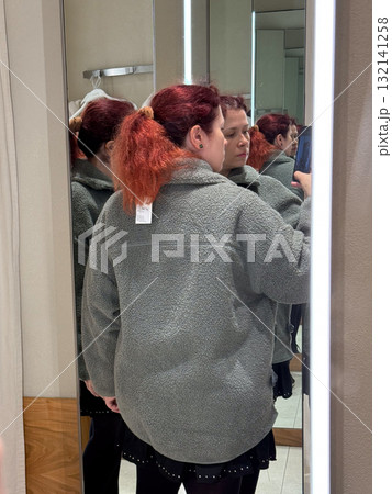 Woman in gray fleece jacket posing in fitting room mirror, back view. Expression of modern comfort, neutral elegance, and quiet confidence in minimalist fashion context. 132141258