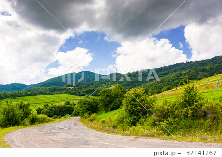 uzhanian pass in carpathian mountain landscape. old asphalt country road take turn downhill near forest. rural scene with field and haystacks in summer under cloudy sky. countryside travel background uzhanian pass in carpathian mountain landscape. old asphalt country road take turn downhill near forest. rural scene with field and haystacks in summer under cloudy sky. countryside travel background 132141267