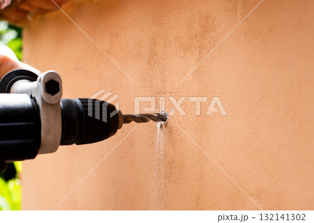 Drilling a hole in a wall with power drill 132141302