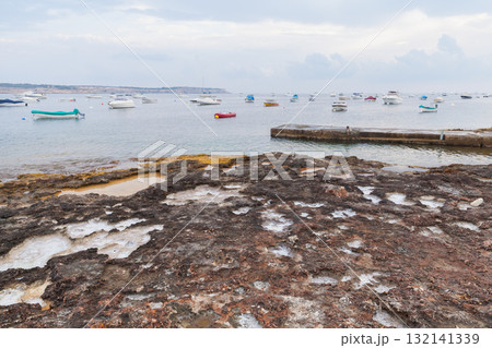 A rocky shoreline leads to a tranquil harbor filled with small boats A rocky shoreline leads to a tranquil harbor filled with small boats 132141339