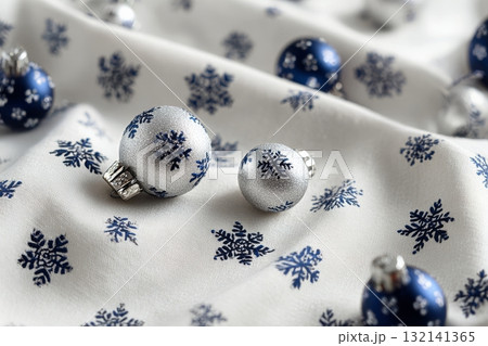 Bright Silver and Blue Christmas Ornaments Resting on Snowflake-Patterned Fabric 132141365