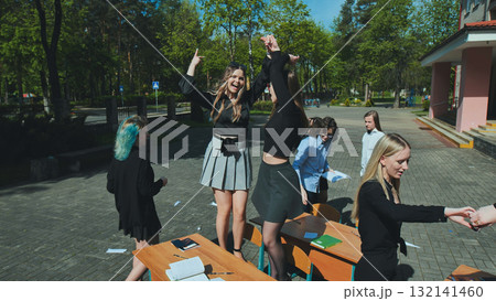 Students joyfully celebrating the end of the school year, standing on desks in the schoolyard, embracing freedom and friendship Students joyfully celebrating the end of the school year, standing on desks in the schoolyard, embracing freedom and friendship 132141460