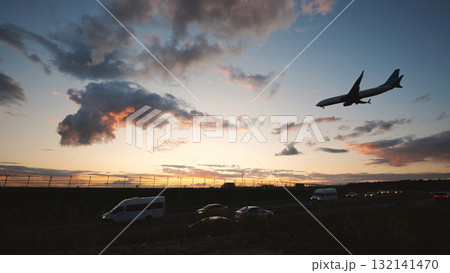 Jet landing at sunset with cars driving on a road near the airport Jet landing at sunset with cars driving on a road near the airport 132141470