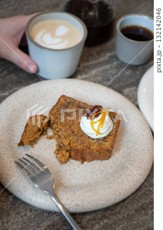 A slice of carrot cake with cream cheese frosting, pecan, and orange zest served with a cup of latte in a cozy cafe A slice of carrot cake with cream cheese frosting, pecan, and orange zest served with a cup of latte in a cozy cafe 132142046