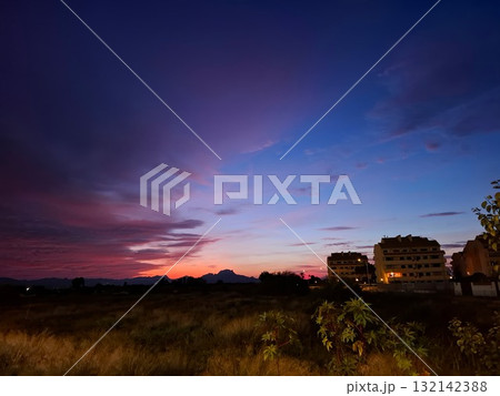 This stunning sunset in southern Spain features a blend of orange, pink, and purple hues filling the sky. Buildings softly outline the horizon, creating a serene scene. 132142388