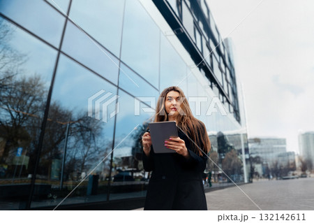 Young Woman Using Tablet While Standing on Urban Street With Modern Buildings and Reflection During a Clear Day Young Woman Using Tablet While Standing on Urban Street With Modern Buildings and Reflection During a Clear Day 132142611