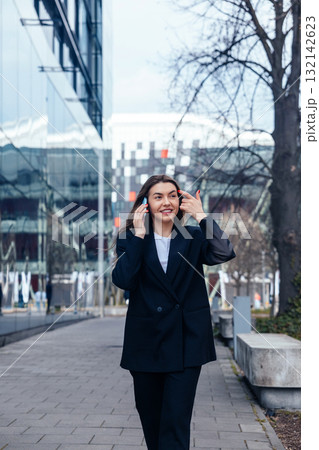 Businesswoman Walking Confidently on Urban Street While Talking on Her Phone During a Sunny Day in a Modern City Environment 132142623