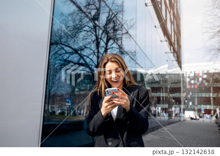 Young woman smiling while using smartphone outdoors in urban setting reflecting modern lifestyle and technology engagement concept 132142638