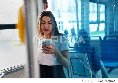 Young woman using smartphone in public transport setting, reflecting on glass, engaged in digital communication, modern lifestyle concept 132142682