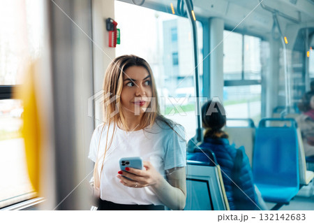 Young woman using smartphone while traveling on public transport, enjoying the journey and observing surroundings, urban lifestyle concept 132142683