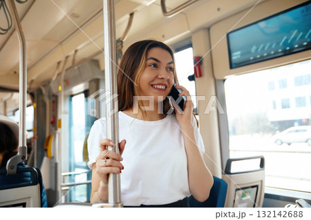 Young woman smiling while talking on smartphone inside public transport bus enjoying her commute with a sense of connection and community concept Young woman smiling while talking on smartphone inside public transport bus enjoying her commute with a sense of connection and community concept 132142688