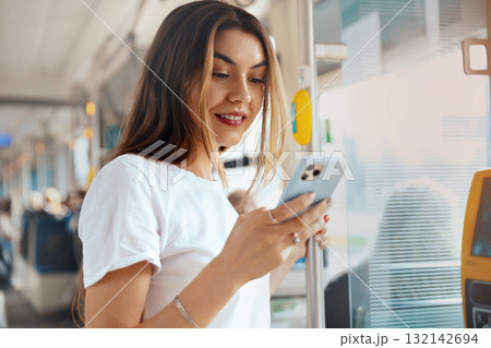 Young woman using smartphone while traveling on public transport, enjoying her time and connecting with others, modern lifestyle concept 132142694