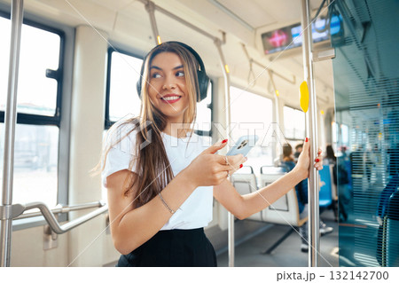 Young woman enjoying music on public transport while holding smartphone, smiling and looking around, urban lifestyle concept Young woman enjoying music on public transport while holding smartphone, smiling and looking around, urban lifestyle concept 132142700