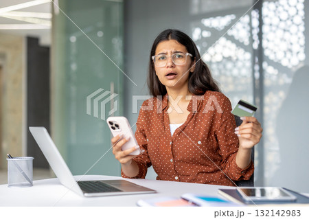 Woman holding a credit card and telephone, looking shocked and experiencing a payment error or fraud issue while trying to make an online purchase using a laptop Woman holding a credit card and telephone, looking shocked and experiencing a payment error or fraud issue while trying to make an online purchase using a laptop 132142983